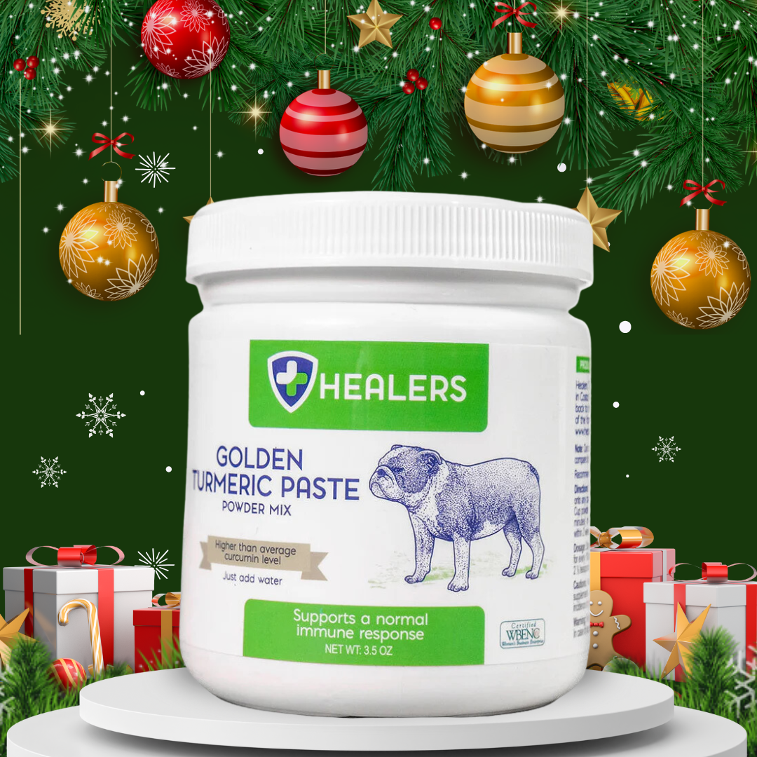 White jar of Healers Golden Turmeric Paste with bulldog label, surrounded by Christmas ornaments, snowflakes, and gift boxes. Holiday-themed product image.